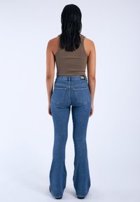Vaqueros azules acampanados de mezclilla con cintura alta, con una etiqueta en la parte posterior y dos bolsillos traseros, combinados con una camiseta sin mangas marrón.