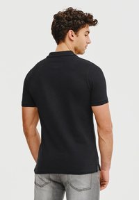 Czarna koszulka polo o dopasowanym kroju, z krótkimi rękawami i subtelną fakturą. Posiada klasyczny kołnierzyk oraz boczne rozcięcia u dołu.
