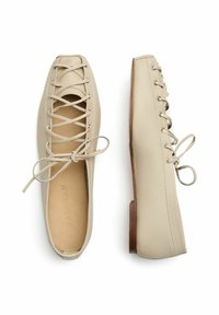 Beige kožené baleríny s kulatou špičkou, dekorativními tkaničkami a plochým dřevěným podpatkem. Hladký materiál s vnitřním logem.