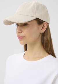 Light beige cap made of herringbone fabric, featuring a curved brim and a structured upper. Worn with a white crew-neck shirt.