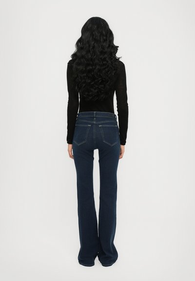 Jeans acampanados de color azul oscuro con un ajuste ceñido en la cintura y una pierna ligeramente suelta. Cuenta con cinco bolsillos y detalles de costura en la parte trasera.