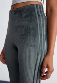 Gray ribbed leggings made of soft velour with a high waist, featuring tonal side stripes and a small logo detail near the waistband.