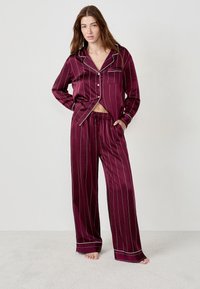 Burgundy pyjamaset i mjuk tyg med vita vertikala ränder, en knapplistopp med ficka och byxor med dragsko i midjan.
