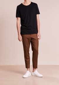Camiseta negra de manga corta, pantalones marrones ajustados y zapatillas blancas. Tejido suave, escote redondo, diseño ceñido.