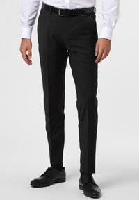 Schwarze maßgeschneiderte Hosen mit geradem Schnitt, flachem Bund und minimalistischem Design. Getragen mit einem hellen Hemd und schwarzen Schnürschuhen.