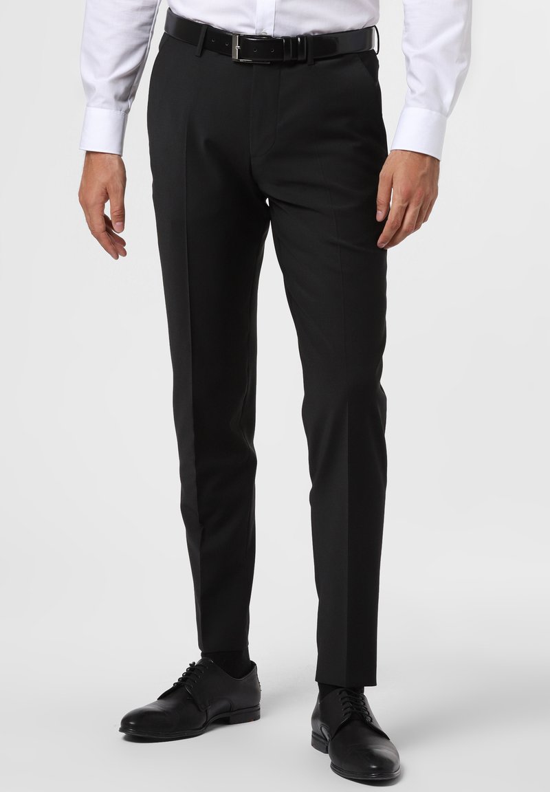 Schwarze maßgeschneiderte Hosen mit geradem Schnitt, flachem Bund und minimalistischem Design. Getragen mit einem hellen Hemd und schwarzen Schnürschuhen.