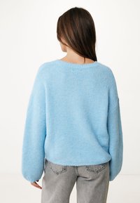 Lichtblauwe, comfortabele gebreide trui met verlaagde schouders en een relaxte pasvorm. Geribbelde ronde halslijn en brede mouwen, gecombineerd met grijze jeans.