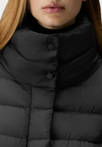 Zwarte donzige jas met hoge kraag, voorzien van een horizontaal doorgestikt ontwerp en twee zwarte knopen aan de voorkant. Gladde, glanzende textuur.