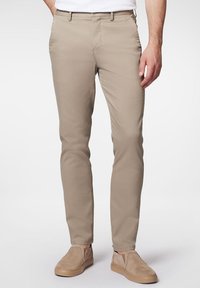 Beżowe chinosy wykonane z tkaniny żakardowej, w slim fit, z przednimi kieszeniami i zapięciem na zamek. Połączone z jasnobeżowymi butami typu slip-on.
