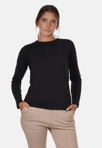 T-shirt nero a maniche lunghe con scollo rotondo e design aderente. Tessuto morbido con dettagli minimi, indossato sopra pantaloni beige.