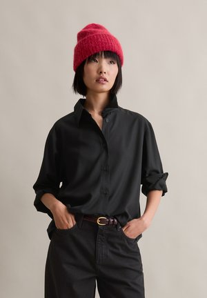 Black button-up shirt with a relaxed fit, featuring rolled sleeves and a collar, paired with high-waisted dark pants and a red knit beanie.