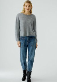 Grijze fuzzy trui met lange mouwen, gecombineerd met losse blauwe denim jeans met flapzakken en een ontspannen pasvorm. Zwarte kniehoge laarzen.