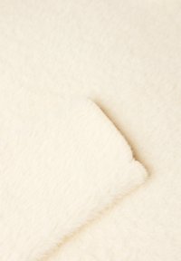 Cremefarbenes, flauschiges Material mit einer weichen Textur, das einen glatten Rand aufweist und ein leichtes, warmes Aussehen hat.