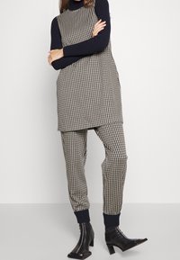 Tunique en tissu vichy noir et beige, assortie à des joggeurs vichy. Design col roulé, poignets côtelés et bottines noires.