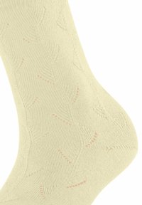 Kremowa, dziergana skarpetka z misternymi, zygzakowatymi i kropkowanymi wzorami koronki pokrywającymi kostkę i stopę.