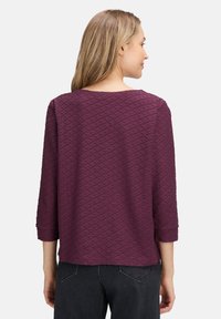 Haut bordeaux en tissu texturé à motif en diamant, décolleté arrondi et manches trois-quarts, associé à un jean noir.