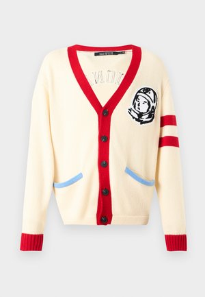 Crème gekleurde cardigan met een rode V-hals, geribbelde manchetten en blauwe accentzakken. Voorzien van een astronautborduring op de linkerborst. Zes zwarte knopen.