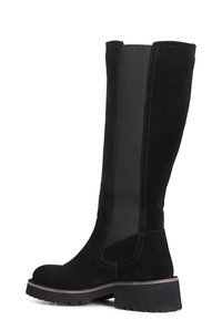 Botas negras hasta la rodilla con textura de ante, paneles laterales elásticos y una suela de goma gruesa con detalles acanalados.
