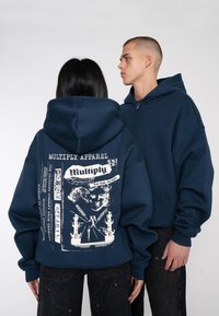 Sweat-shirt à capuche bleu marine avec un grand imprim�é graphique au dos, comportant des textes et des illustrations de navires ; design ample avec fermeture éclair à l'avant.