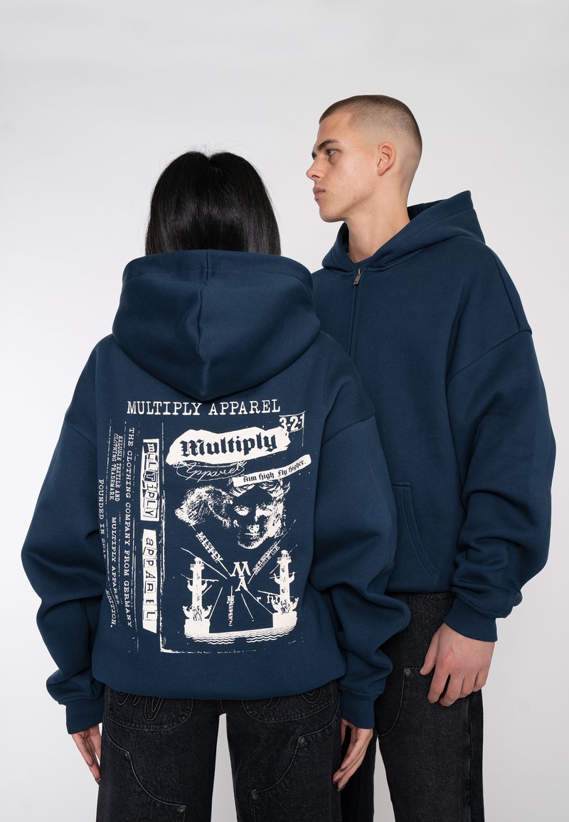 Sweat-shirt à capuche bleu marine avec un grand imprimé graphique au dos, comportant des textes et des illustrations de navires ; design ample avec fermeture éclair à l'avant.