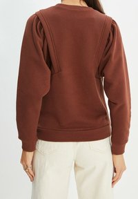 Sweat-shirt marron avec épaules bouffantes, col ras du cou et poignets côtelés. Le tissu a une texture lisse, présentant une coupe décontractée et des lignes épurées.