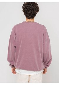 Felpa oversized color lilla con una texture morbida, vestibilità rilassata e colletto a costine. Presenta spalle scese e maniche con polsini.
