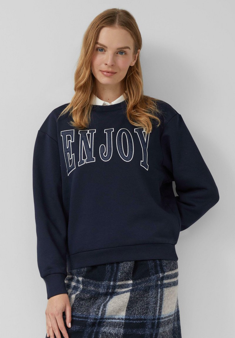 Sudadera azul marino con la palabra "ENJOY" en letras blancas. Tiene un cuello redondo y puños acanalados. Combina con una falda de cuadros en tonos gris y azul.