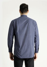 Camicia a maniche lunghe di colore blu navy con un piccolo motivo a quadretti. Presenta un colletto rigido e polsini abbottonati. Tessuto di cotone con una texture morbida.
