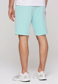 Lichtblauwe katoenen shorts met een klassieke snit, voorzien van zijzakken en een achterzak; aangevuld met witte sneakers.