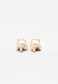 Zapatos de tacón Beige con un upper de tela texturizada y acentos metálicos brillantes. Cuentan con una correa en la parte trasera y un tacón estrecho, suela lisa.