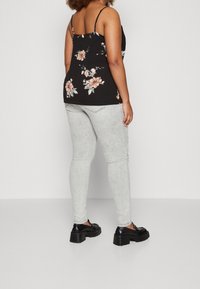 Svart blommig linne med tunna axelband, prydat med rosa och vita blommor. Parat med ljusgrå skinny jeans och svarta kraftiga skor.