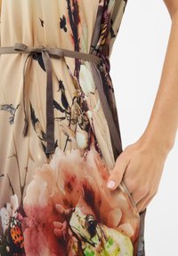 Květinové šaty s lehounce béžovým podkladem, na kterém jsou žáby, květiny a hmyzí motivy. Uvázané v pase tmavohnědým páskem, texturovaná tkanina.