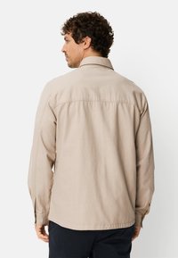 Beiges Langarmhemd aus leichtem Stoff, mit geradem Saum, Rückenpasse und Manschetten mit Knopfverschluss.