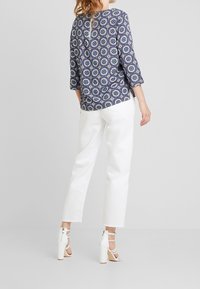 Blusa blu navy a fantasia floreale con maniche a tre quarti, chiusura a chiave sul retro, abbinata a pantaloni bianchi cropped a gamba larga e sandali con cinturino.