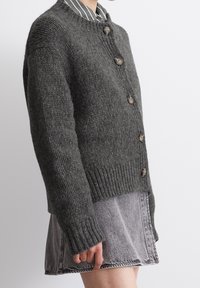 Grijze wollen cardigan met ronde hals, vijf knopen, geribbelde manchetten en zoom, gedragen over een gestreept shirt en een denim rok.