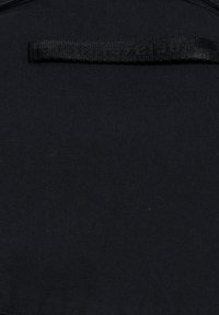 Sort stof med et sort syet mærke, der viser tallene "198810721381" i mørkt tråd nær toppen i midten.