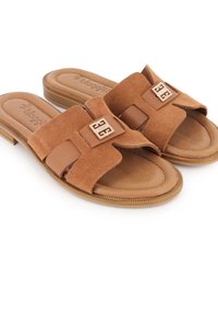 Las sandalias de ante marrón son de tipo slip-on y presentan una tira ancha con cortes, una plantilla acolchada y un sutil acento de logo. Suela plana con borde texturizado.