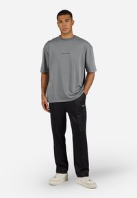 Tricou gri cu mânecă scurtă, cu textul "PEGADOR"; pantaloni de trening negri cu dungi pe laterale; adidași crem. Țesătură fină; croială lejeră; stil casual.