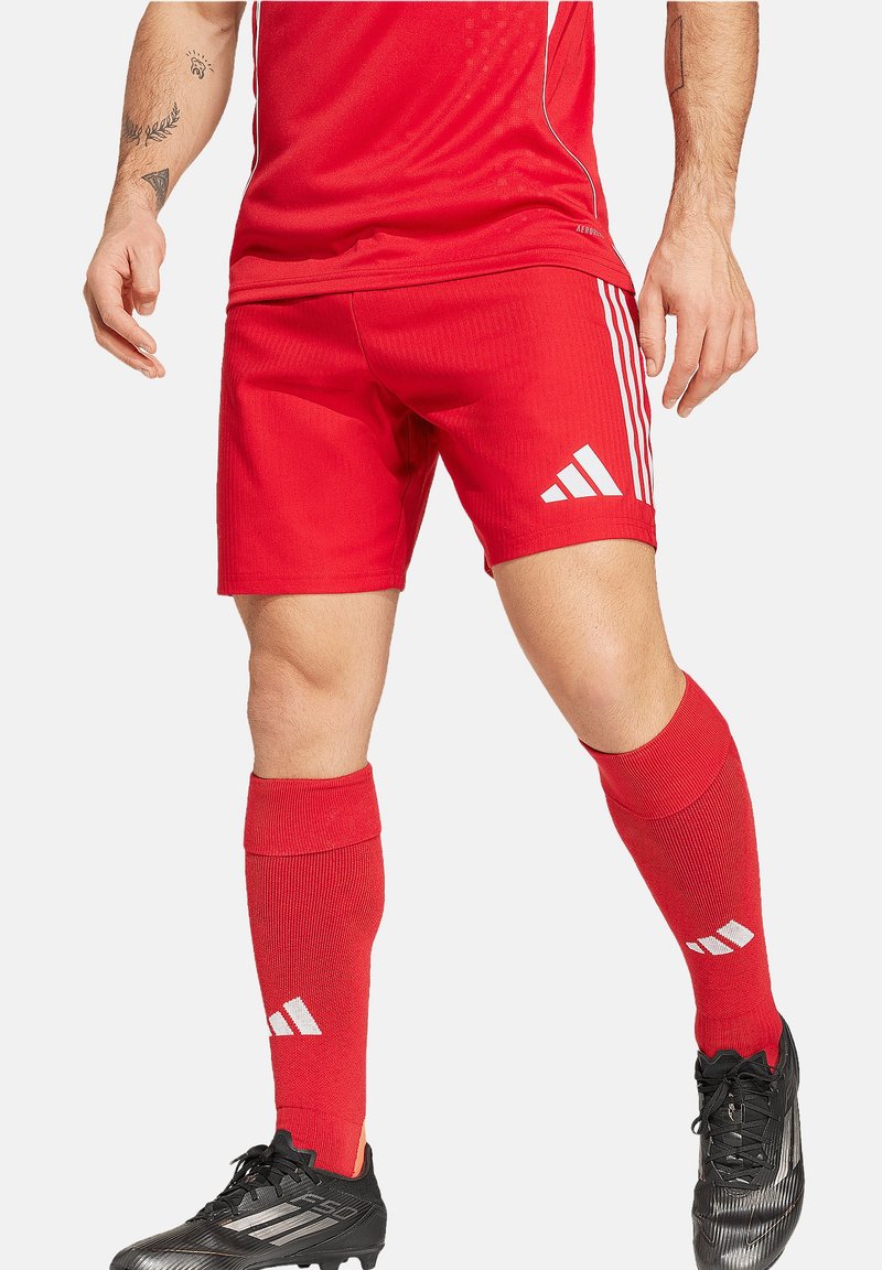 Rote Sportshorts und knielange Socken mit weißen Akzenten. Die Shorts haben drei weiße Streifen am Saum und eine gerippte Textur. Schwarze Fußballschuhe.