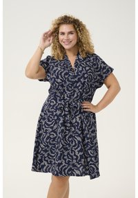 Dunkelblaues Kleid mit einem weißen abstrakten Muster, kurzen Ärmeln, Kragen und einem Bindegürtel in der Taille. Aus leichtem Stoff gefertigt.