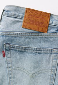 Poche de jean en denim bleu clair avec étiquette en cuir marron Levi Strauss & Co. et étiquette en tissu rouge Levi's.