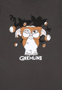Grå t-shirt med et grafik af en tegneseriefigur med store ører, poter der dækker øjnene, og et "Gremlins" logo nedenfor.