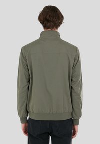 Olivgrön vindtätjacka med hög krage, elastiska ärmslut och ribbad nederkant. Slät yta, lätt material, inga synliga mönster.