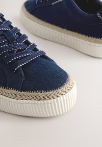 Marineblå lærredsneakers med flettede jute-accenter, hvid gummisål og matchende snørebånd. Tekstureret stof og kontrastsyede detaljer.
