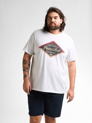 Witte katoenen t-shirt met een rood en zwart ruitpatroon met "Petrol Ind." op de voorkant, gecombineerd met marineblauwe shorts.