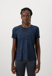 Marineblå t-shirt med korte ærmer i et struktureret slangeskinds mønster, rund halsudskæring og blødt stof. Pasformen er afslappet og velegnet til hverdagsbrug.