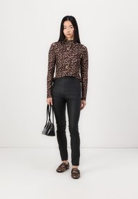 Top met luipaardprint en lange mouwen, gecombineerd met hoge zwarte skinny jeans. Het model houdt een kleine zwarte handtas vast en draagt luipaardprint ballerina's.