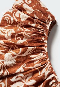 Tissu marron avec des motifs floraux et de feuilles blancs, rassemblé et élastiqué le long d'un bord, suggérant une manche ou un détail de vêtement.