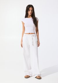 White fitted cap sleeve top with a round neckline paired with lightweight, loose-fitting white trousers. Sandals with brown accents.