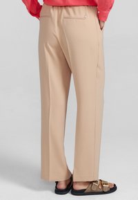 Beige vida byxor med en slät yta, utrustade med två bakfickor med dragkedjor, ihop med bruna sandaler.